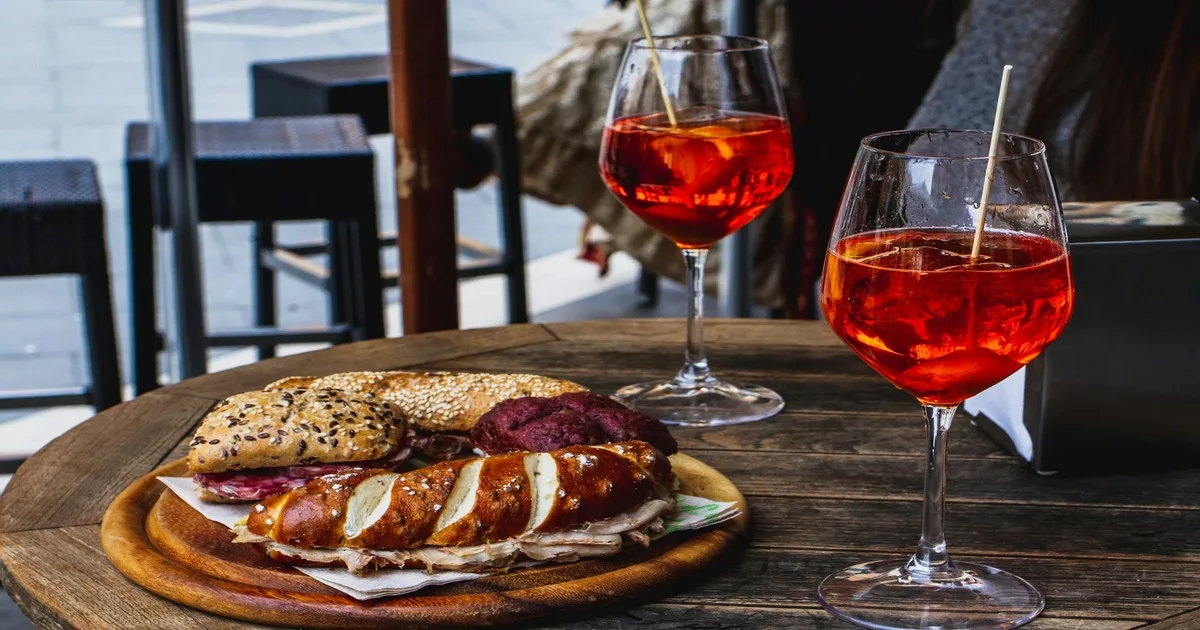 Traditional Venetian food with sandwiches and Aperol spritz drinks on a rustic wooden table.