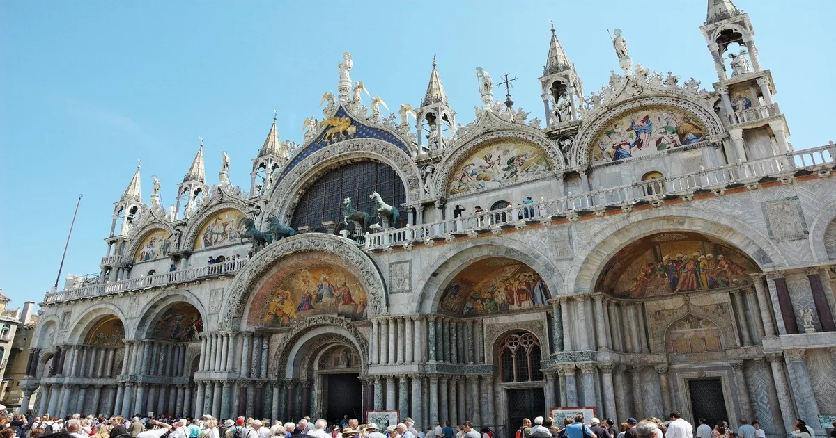 St. Mark’s Basilica in Venice with ornate mosaics and domes under a clear blue sky.
