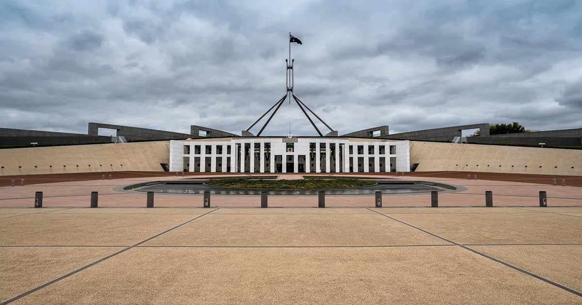 Modern Parliament House in Canberra, Australia, with cloudy sky and Australian flag flying high.