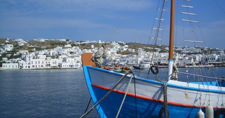 Traditional blue fishing boat moored in Mykonos harbour with whitewashed houses in the background